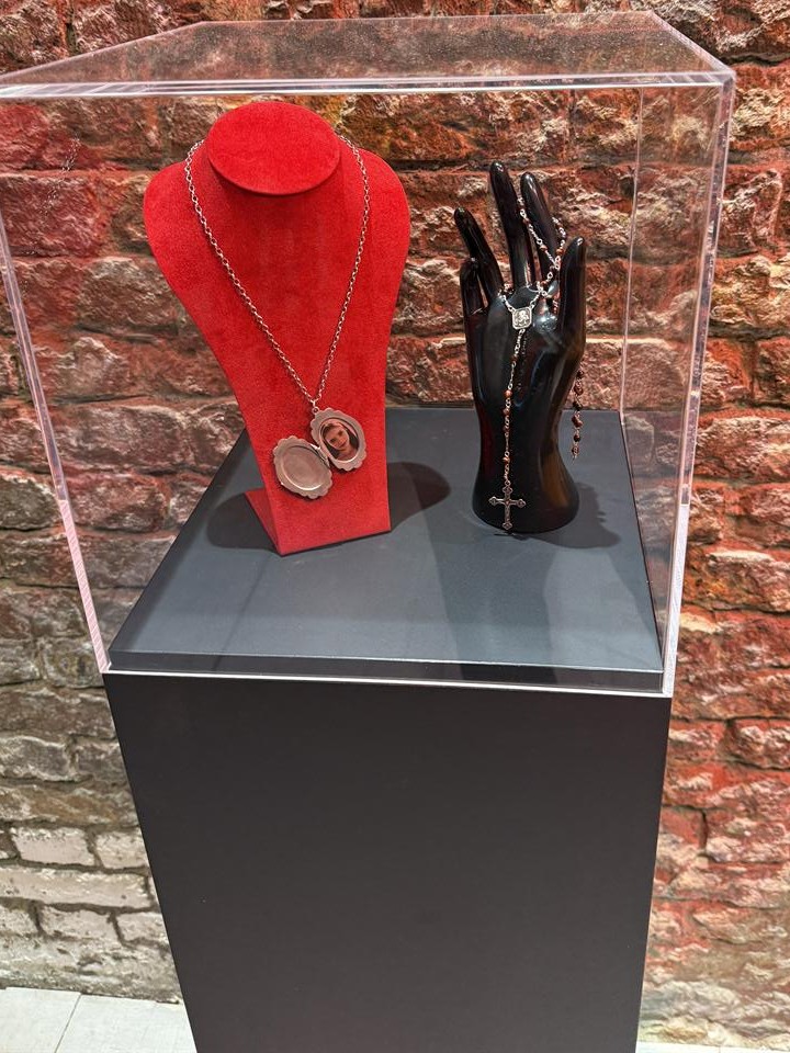 Red jewellery display and black glove holding a rosary inside a clear case
