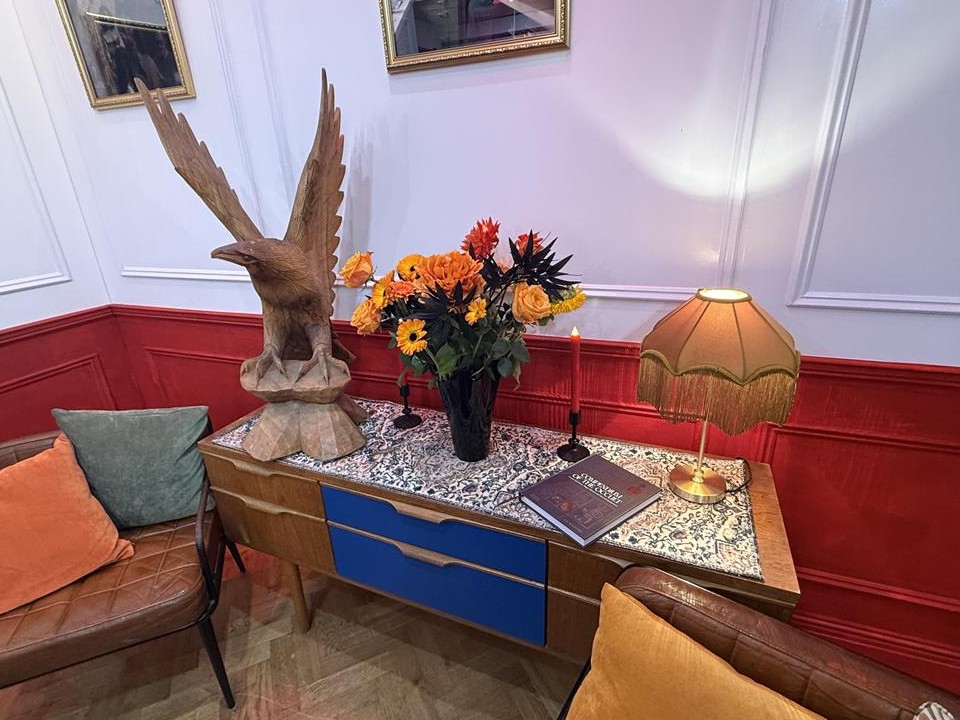 Styled interior room with eagle sculpture, flowers, lamp, and decorative furniture.